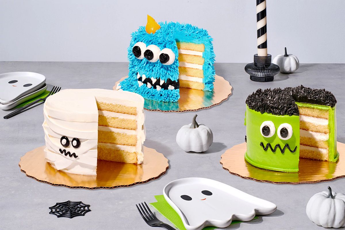 Halloween mini cakes decorated like Frankenstein, a mummy, and a blue monster on a decorated table