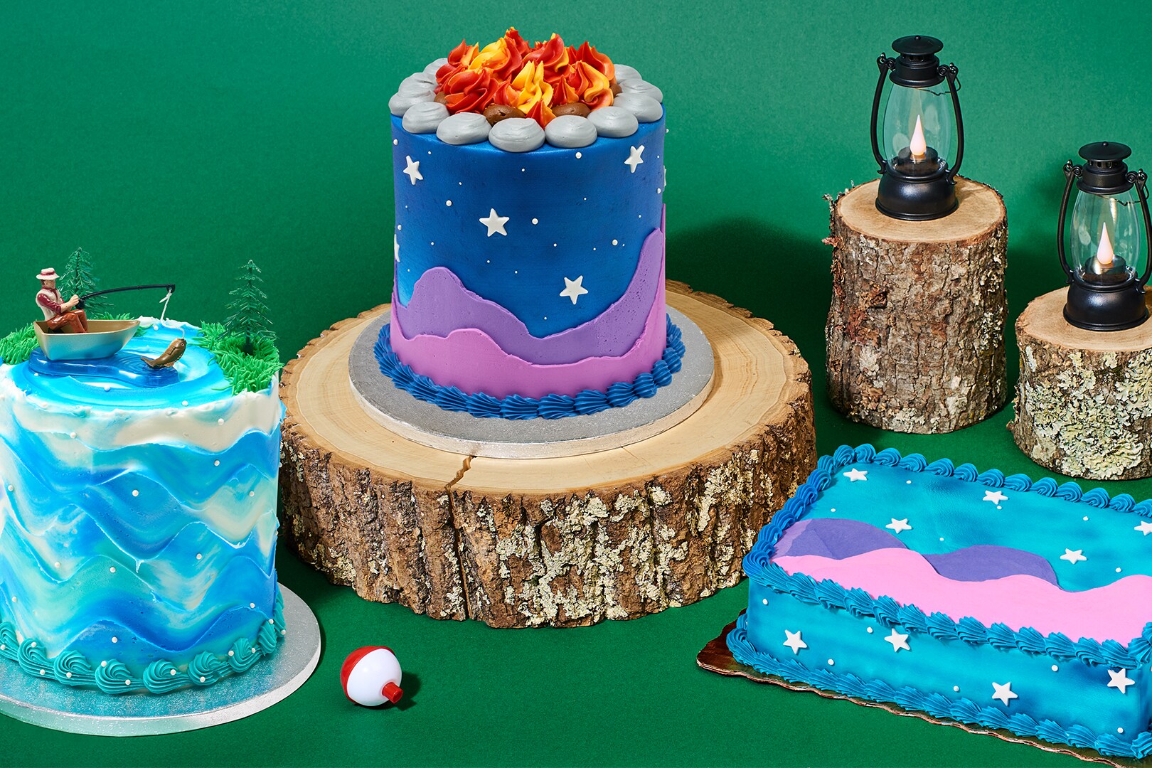 Fishing and camping cakes next to black lanterns on top of small tree stumps
