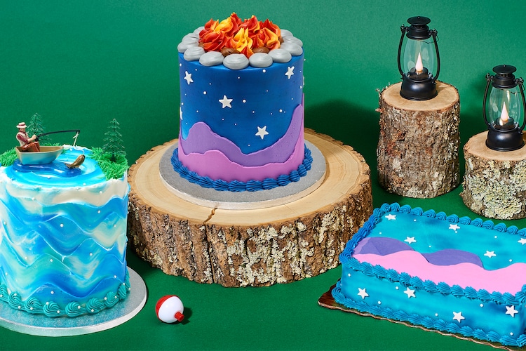 Fishing and camping cakes next to black lanterns on top of small tree stumps