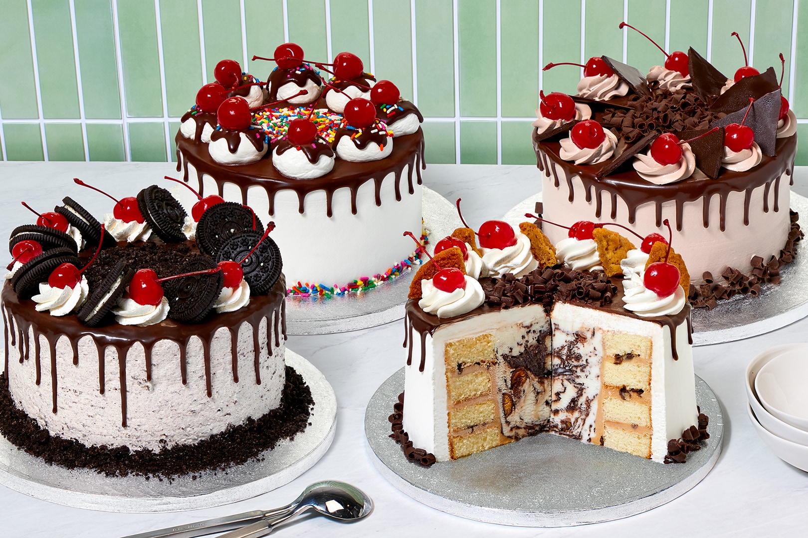 Ice cream cakes on silver trays in front of a green tile background