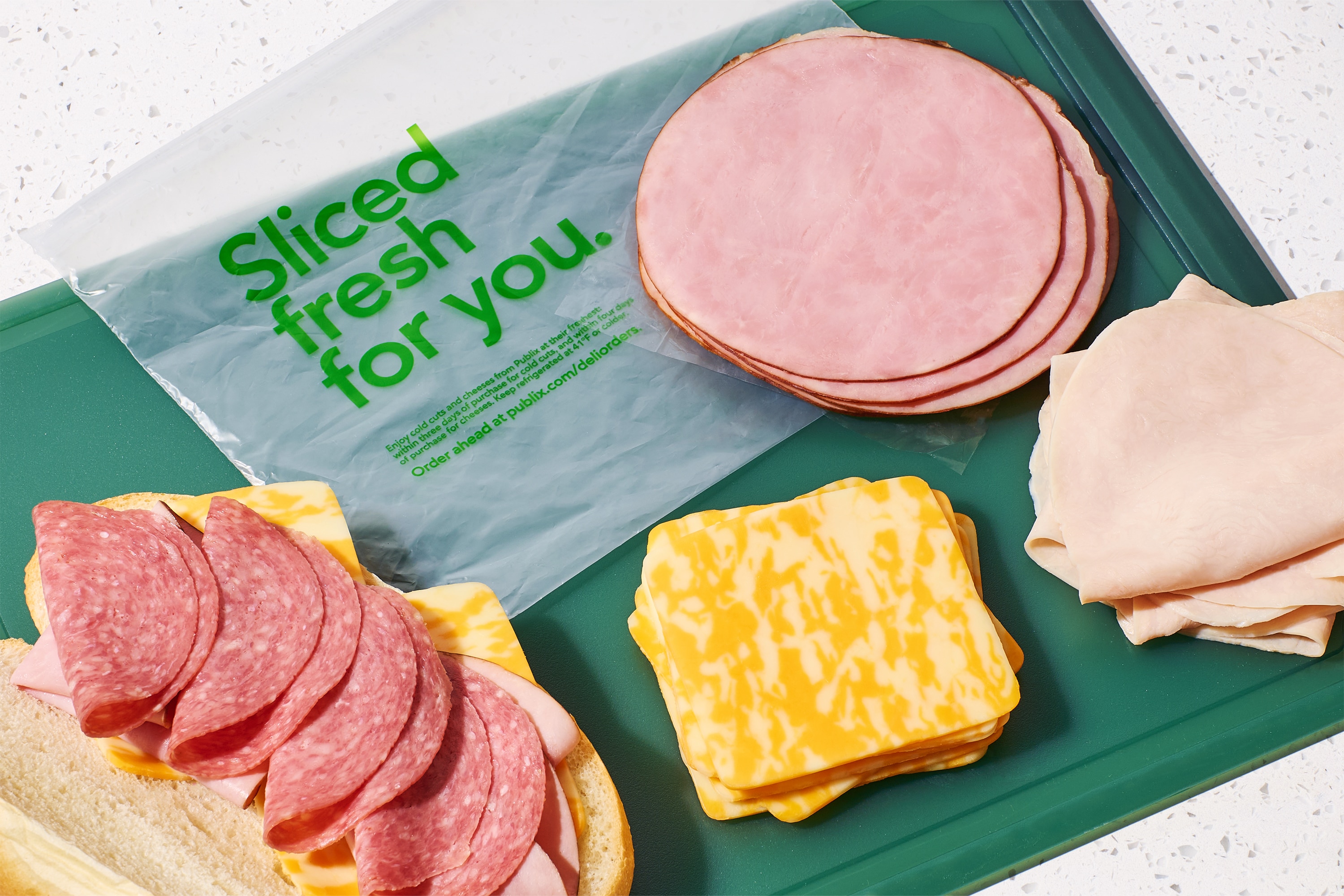 A variety of deli meats and cheese on a cutting board next to an open-face sandwich.