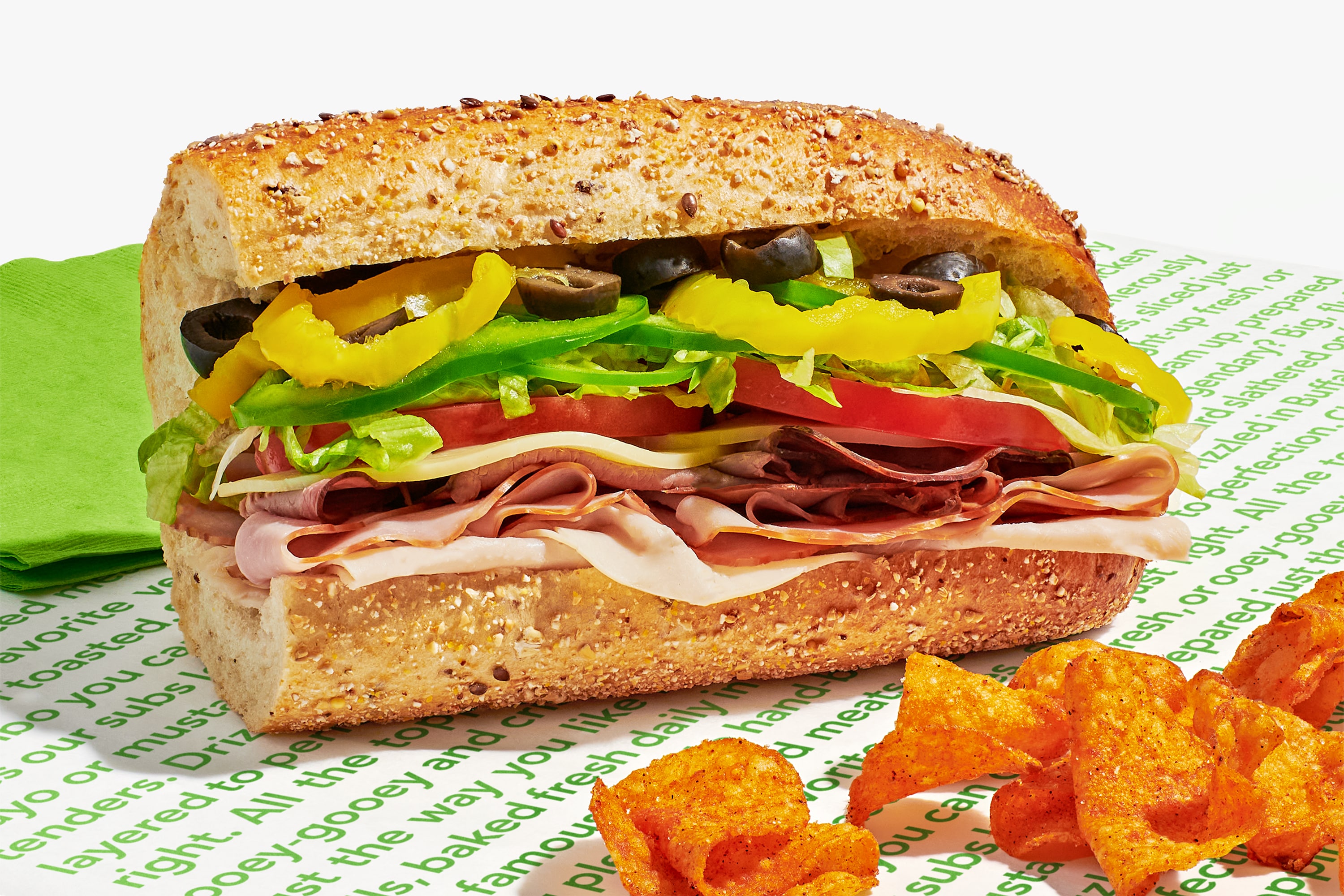 Half of a Publix Ultimate Sub next to some potato chips and napkins.