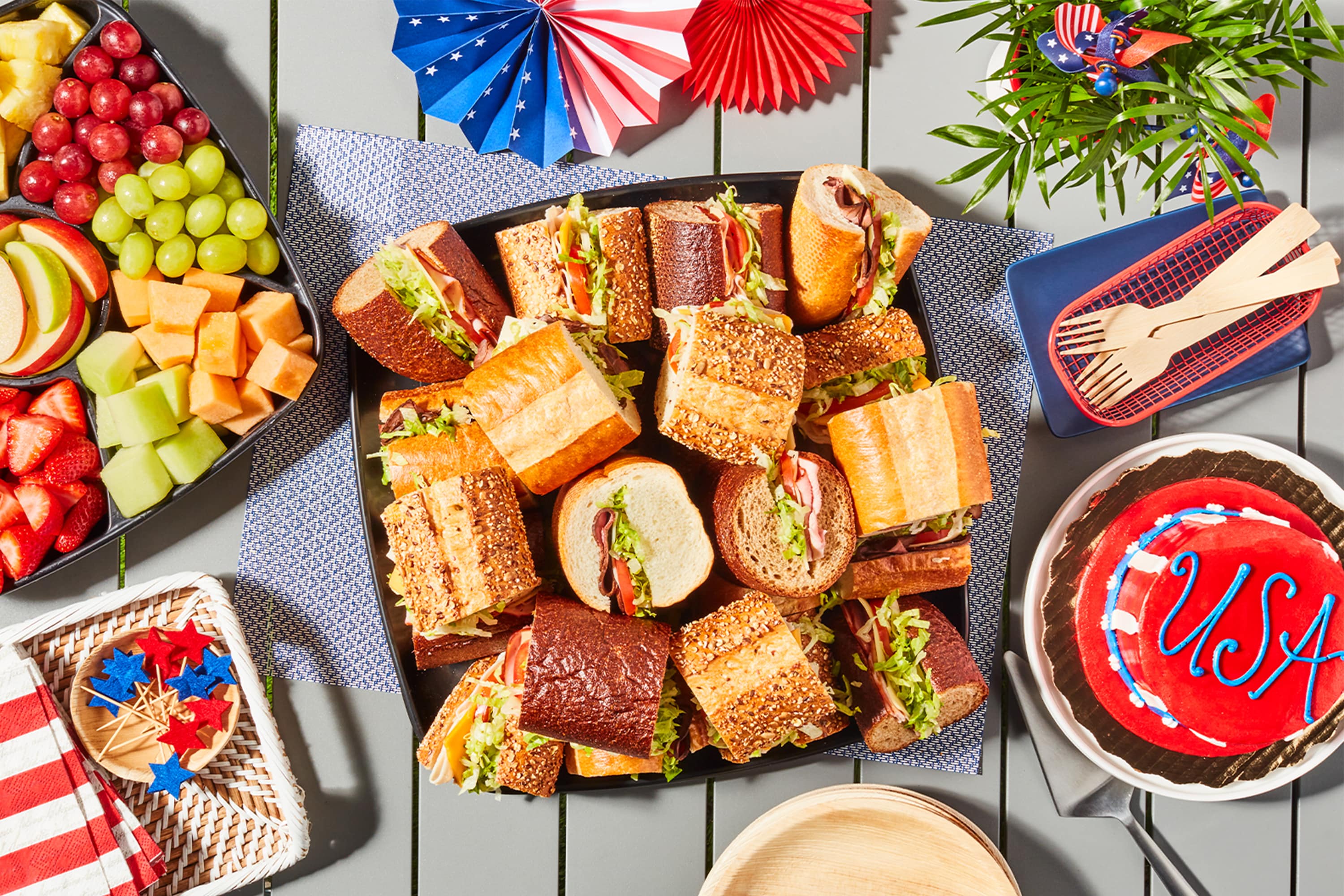 Fourth of July tablescape with fruit platter, sub platter, and patriotic cake.