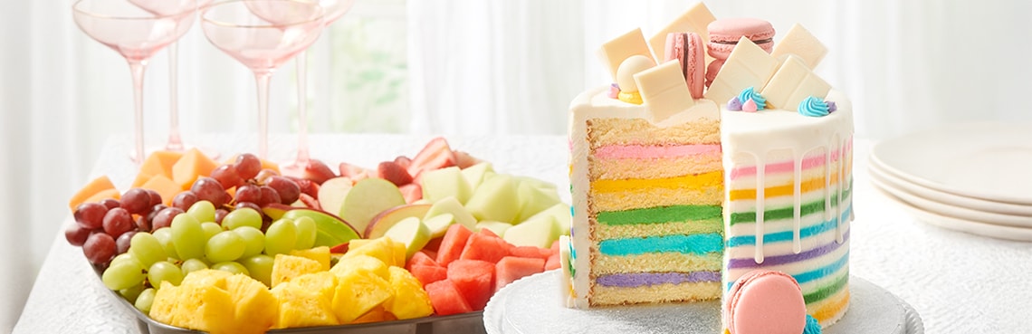 party table with platter of fresh fruit and a colorfully decorated cake