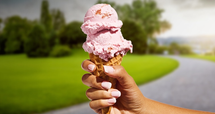 Hand holding strawberry ice cream cone outside.