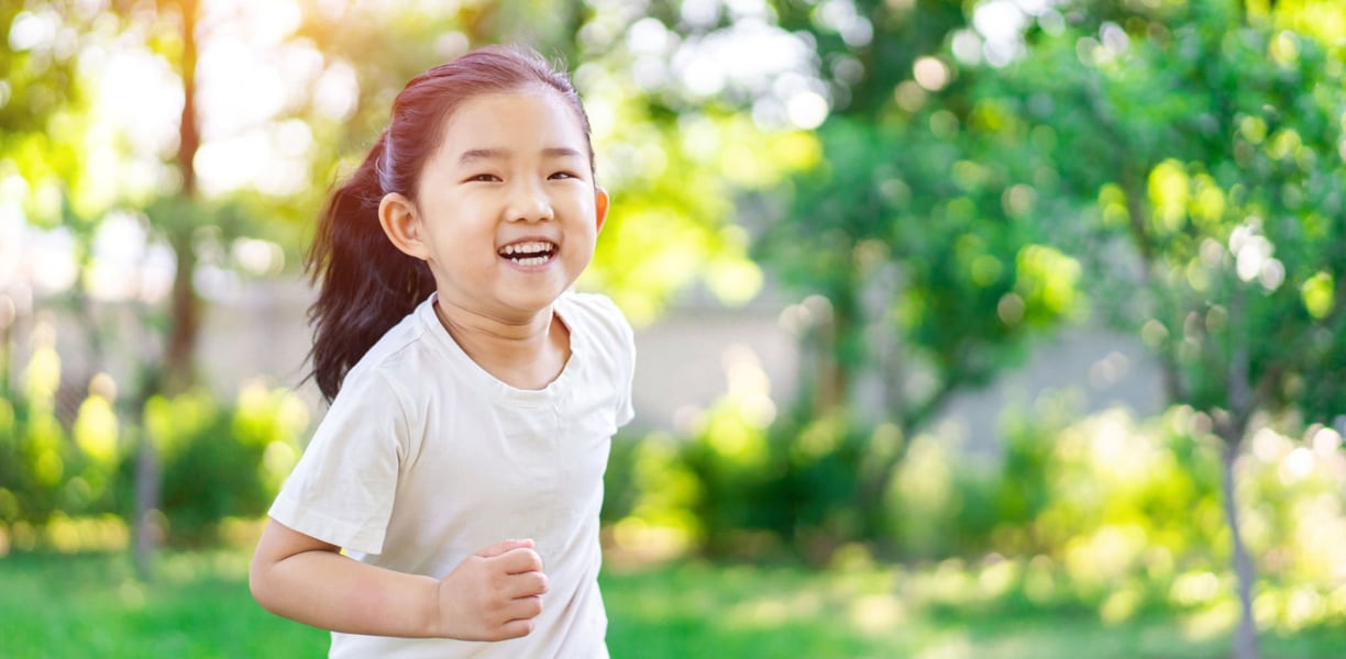 young asian girl running in a grassy field 