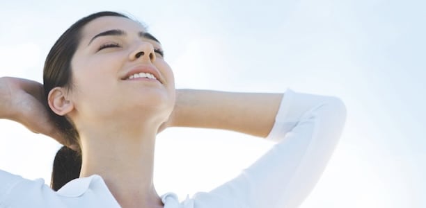 Woman with her eyes closed and head tilted up against a blue sky