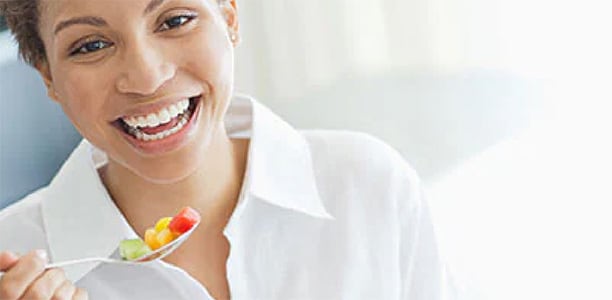 woman eating a a spoon of cut fruit