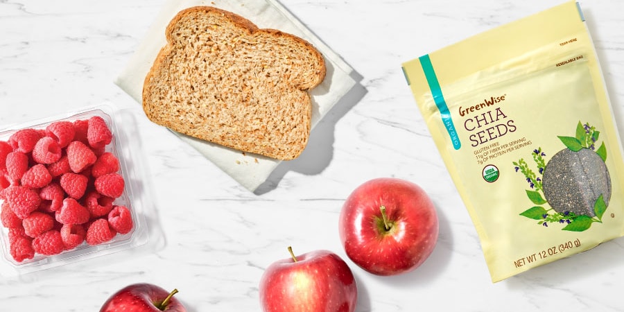 Raspberries, whole grain toast, apples, and GreenWise chia seeds on a clean surface, arranged for a healthy fiber-rich snack.