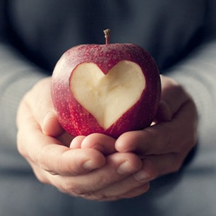 Hands holding an apple with a heart carved into it.