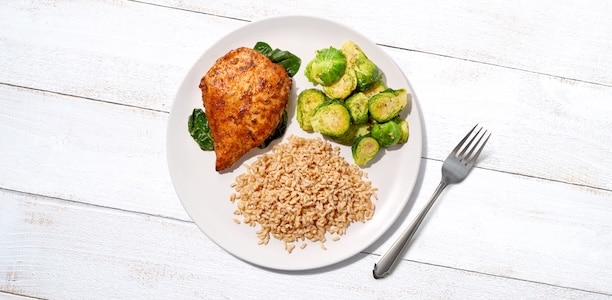 A plate with sofrito-seasoned chicken breast, Brussels sprouts, and brown rice.