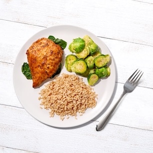 A plate with sofrito-seasoned chicken breast, Brussels sprouts, and brown rice.