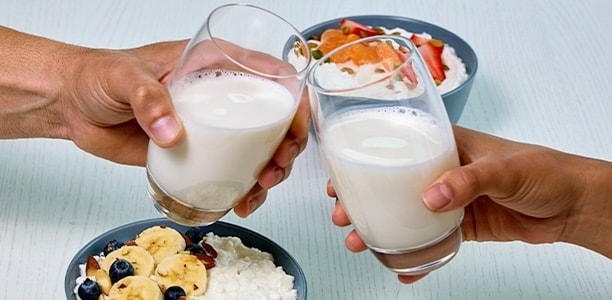 two glasses of milk cheering along with a bowl of cottage cheese with fresh fruit and nuts 