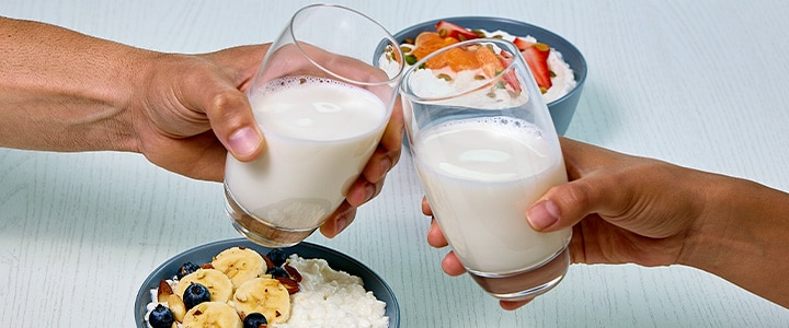two glasses of milk cheering along with a bowl of cottage cheese with fresh fruit and nuts 