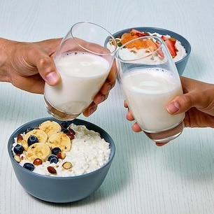 two glasses of milk cheering along with a bowl of cottage cheese with fresh fruit and nuts