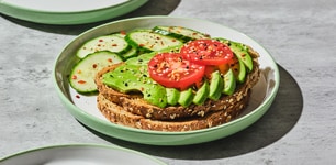 Avocado toast with tomatoes on a plate with fresh cut cucumbers 