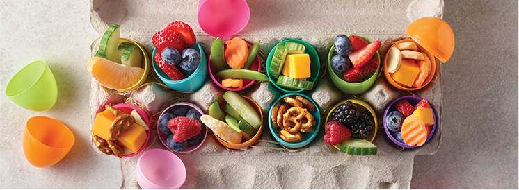 Egg carton with plastic easter eggs that are filled with fruit, vegetables, and other snacks  