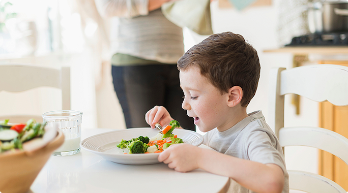 young boy eating a plate of colorful vegetables 