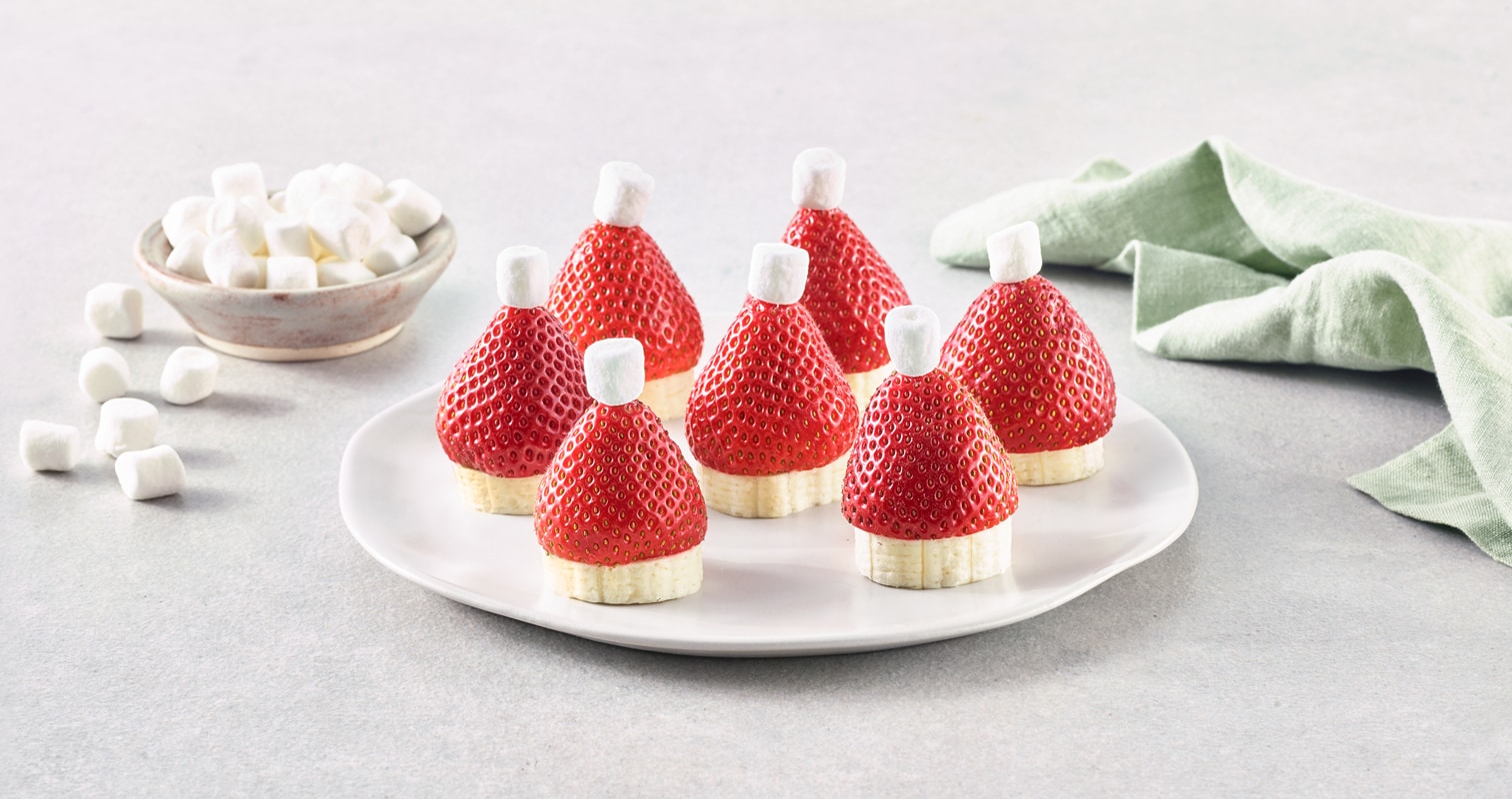 Strawberries, bananas and marshmallows assembled on a plate to look like Santa hats. 