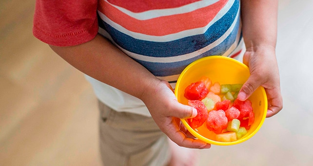 boy holding bowl of cut fruit
