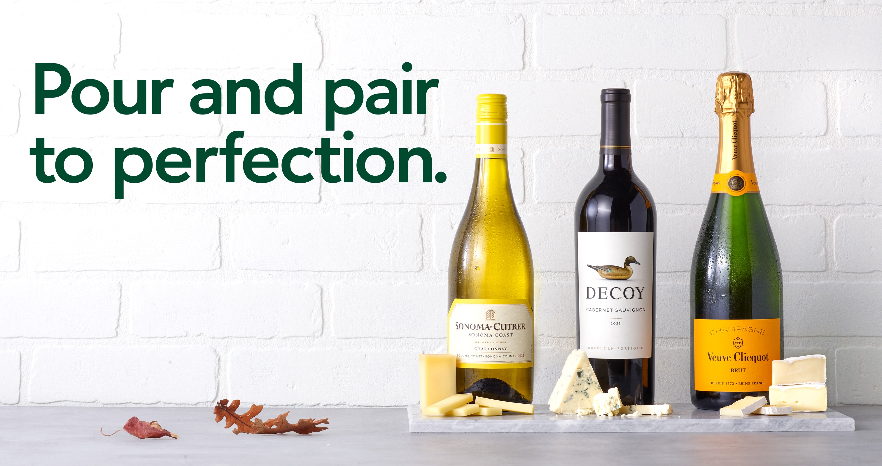 Pour and pair to perfection. Three wine bottles sit on a counter with cheese pairings. 