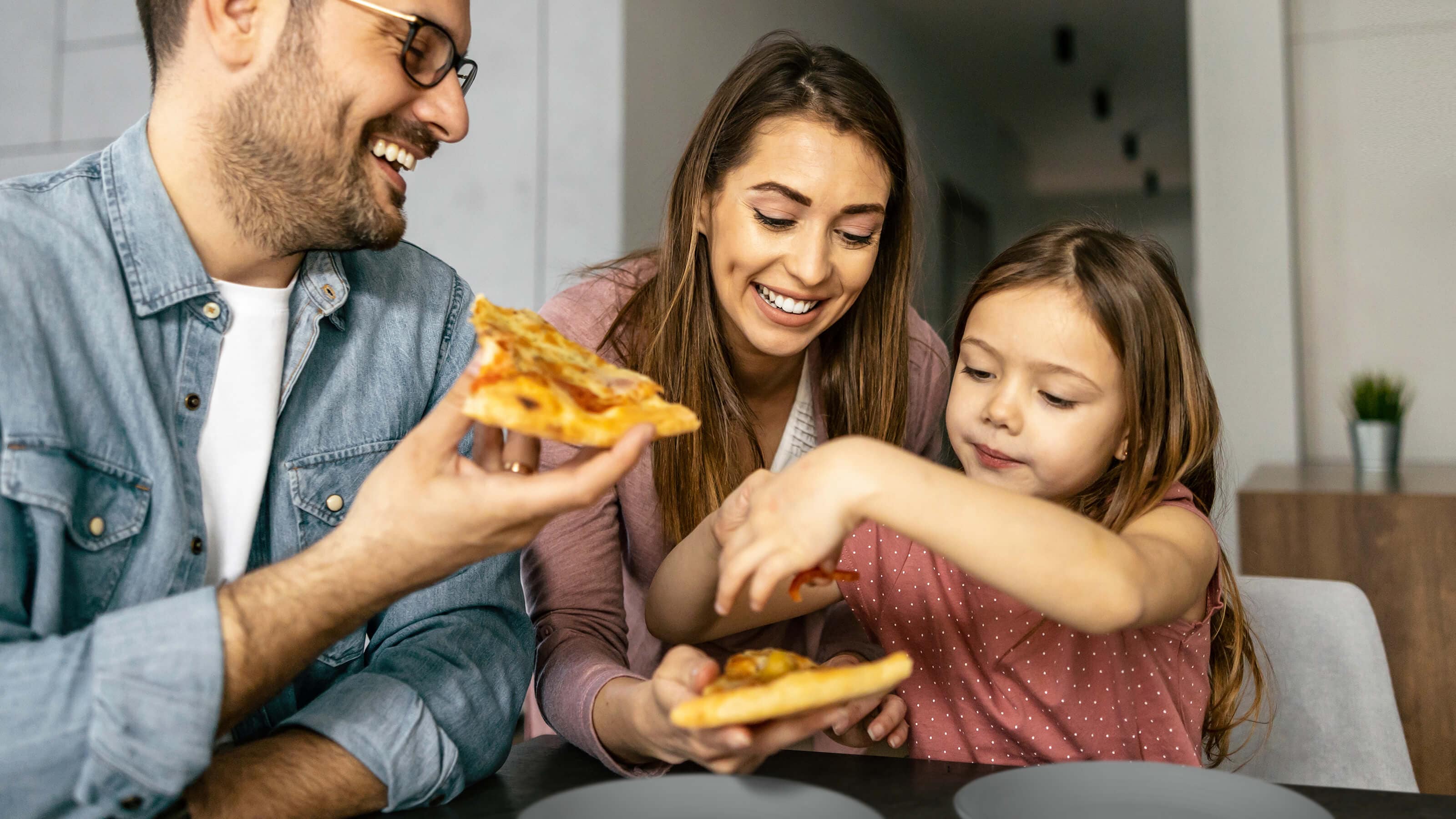 A family enjoying slices of pizza together at a dining table in a cozy home setting.