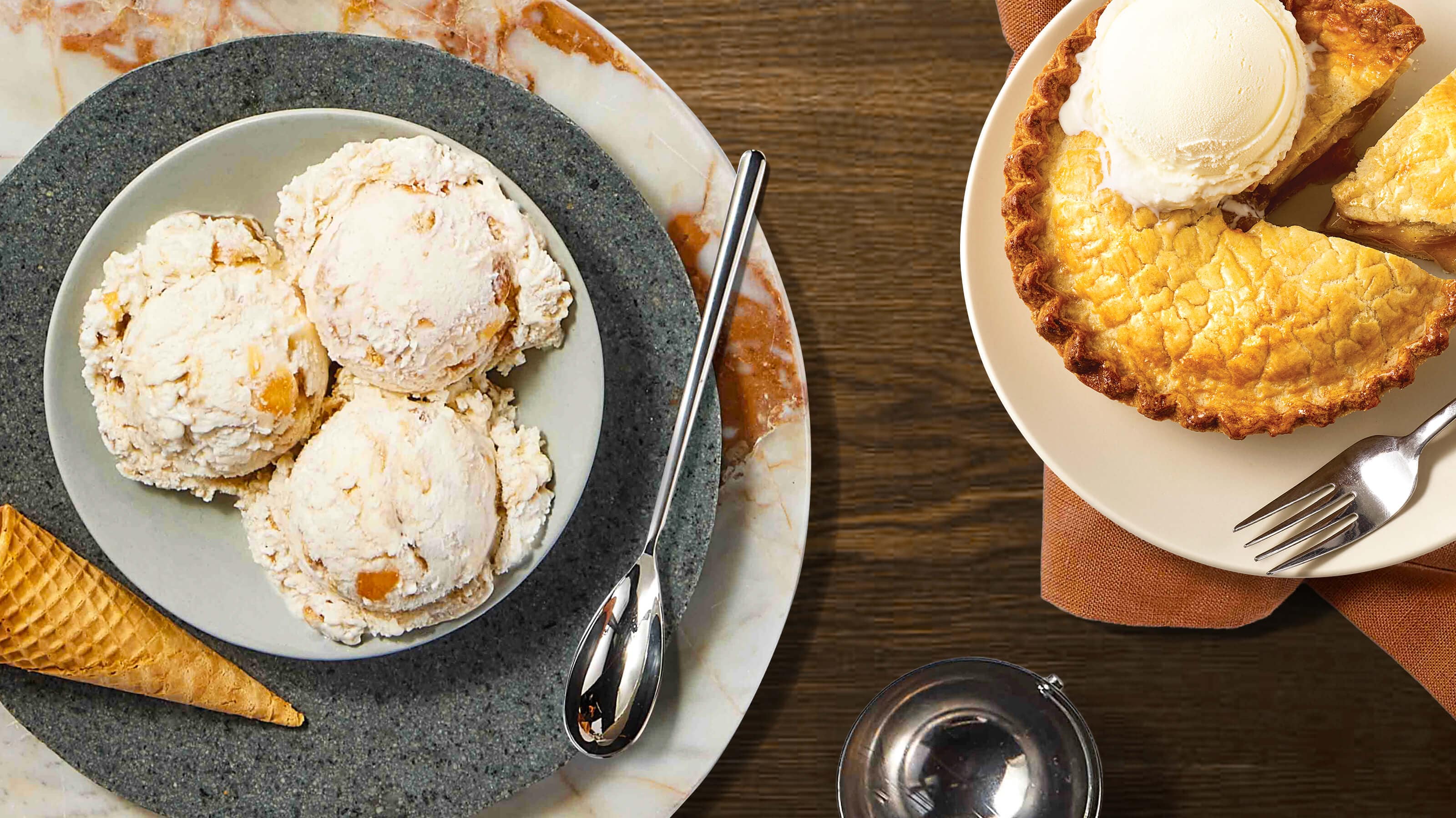 A plate of ice cream scoops with a cone and a spoon beside a sliced pie topped with ice cream on a wooden table.