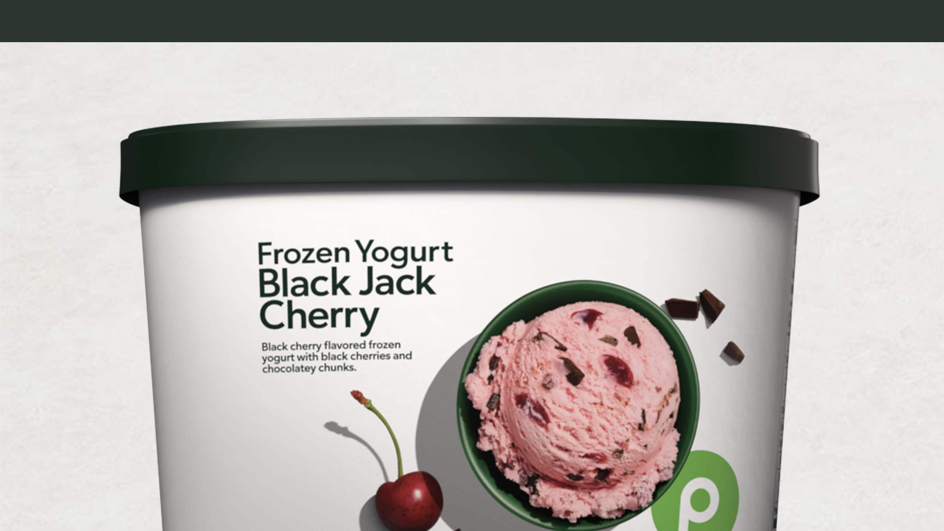 Tub of Publix Black Jack Cherry frozen yogurt with black cherries and chocolate chunks, shown with a cherry and scoop in a bowl.