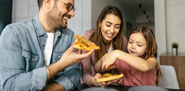 A family enjoying slices of pizza together at a dining table in a cozy home setting.