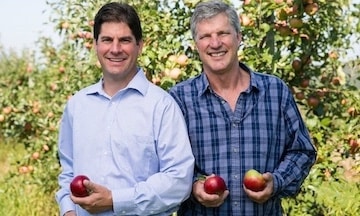 two farmers holding apples in an orchard