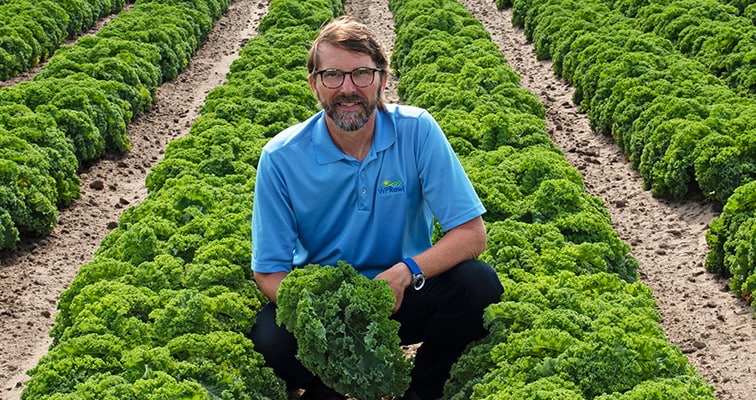 A farmer sitting in a field of fresh greens
