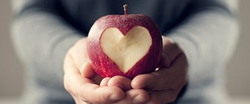 Hands holding an apple with a heart carved into it.