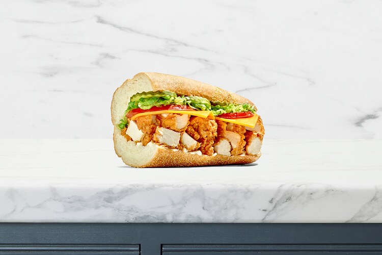 A Publix chicken tender sub with cheese, tomatoes, lettuce, and pickles on a white sub roll.