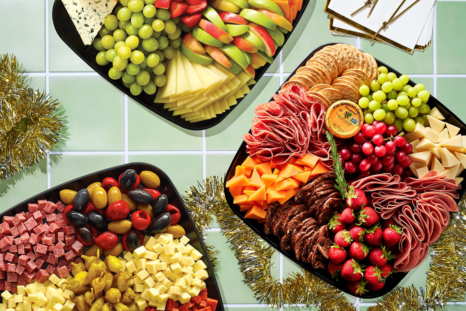 Charcuterie platters and tinsel on a green countertop.