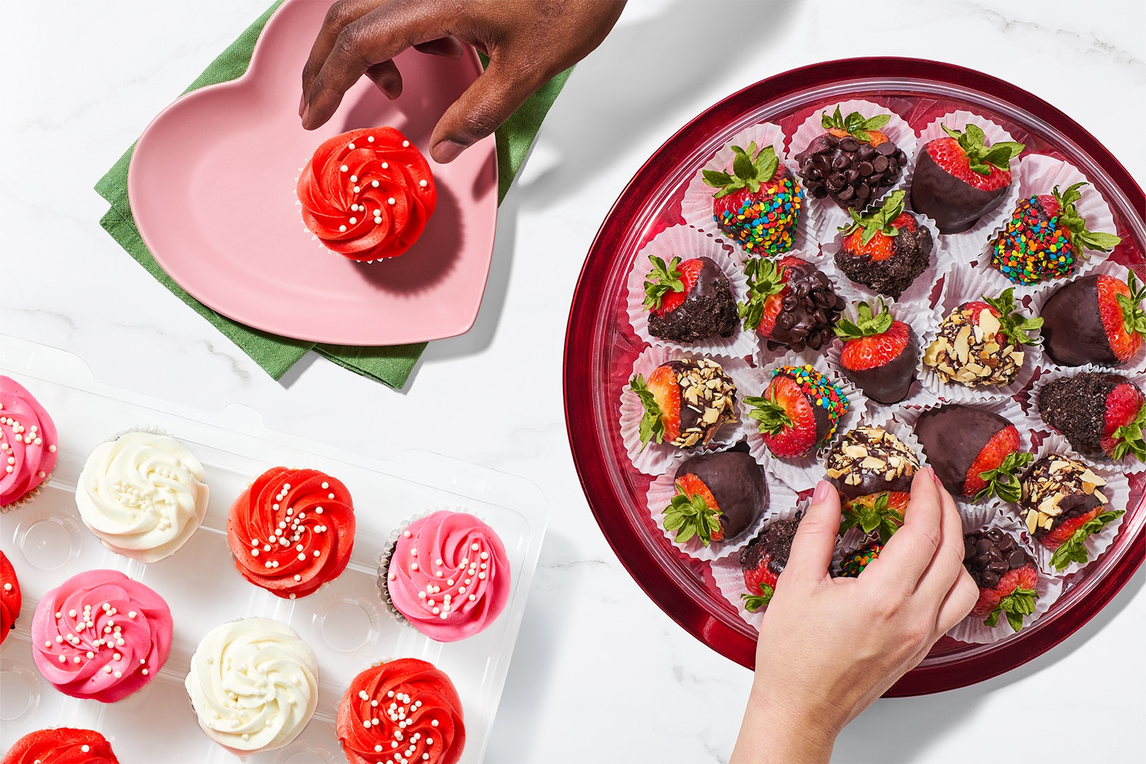 Red, white, and pink Valentine’s Day cupcakes displayed beside a platter of chocolate‑covered strawberries.